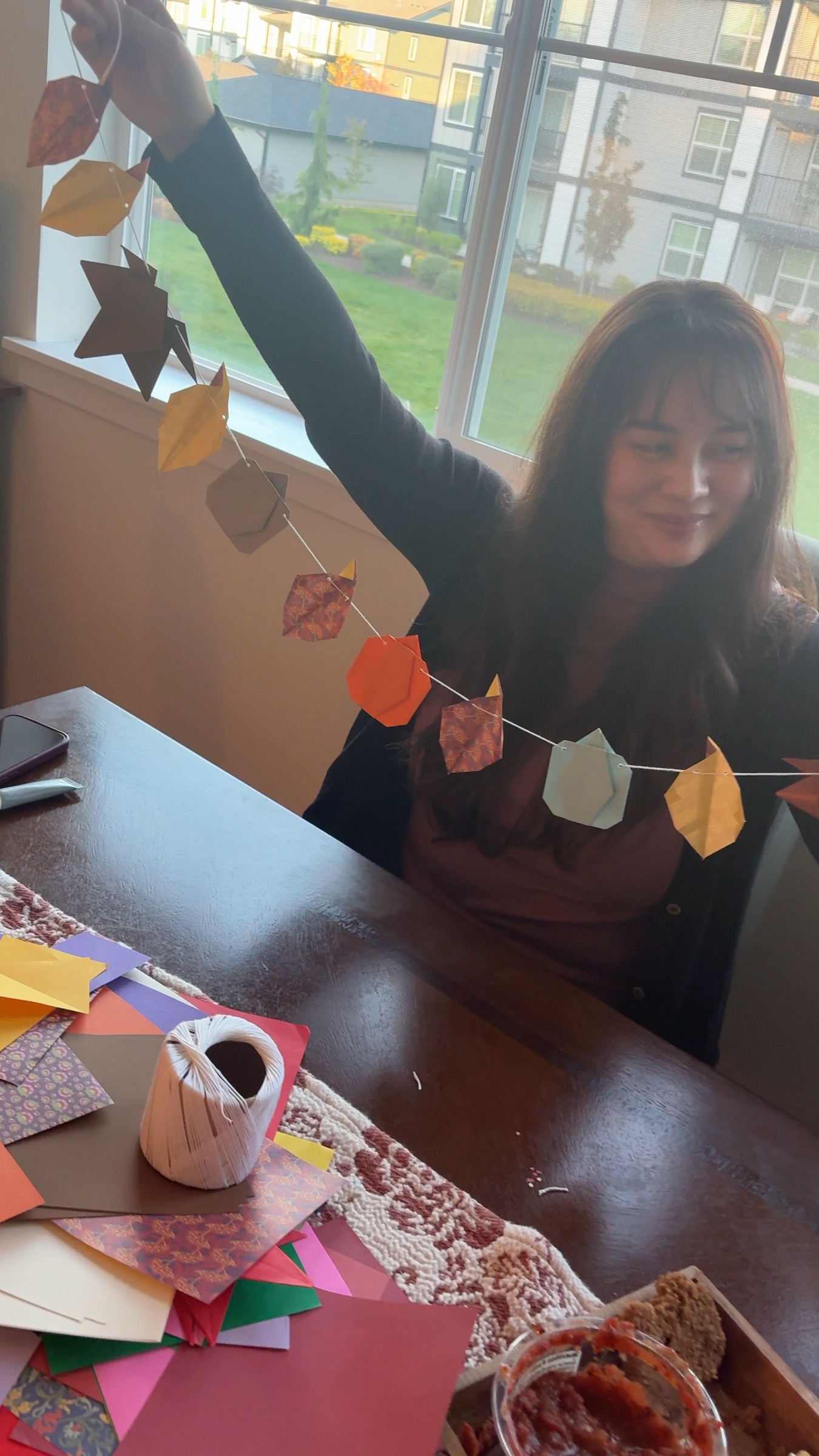 A hand holds up the finished origami garland at the trial night, in front of a sunny window